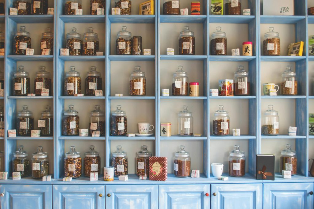 Ein alter, hellblauer Apothekerschrank mit vielen Fächern.
Darin stehen, fein säuberlich geordnet Flaschen verschiedener Größe, mit weißen Etiketten und unerschiedlichen Inhalten.