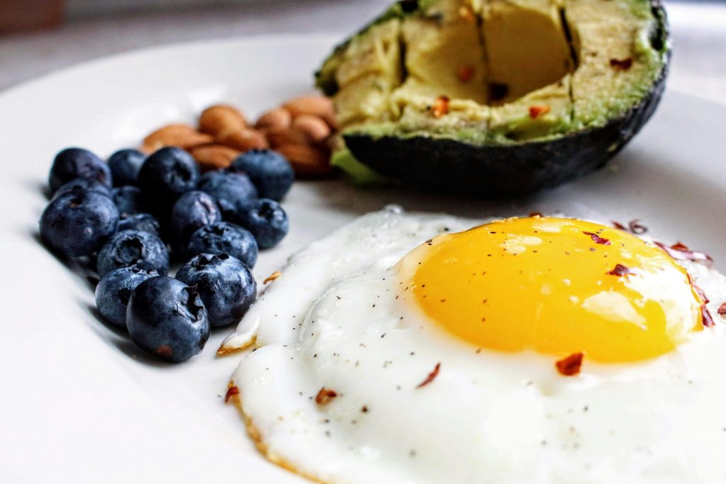 Auf einem weißen Teller liegen Blaubeeren, Mandeln, eine halbe Avocado und ein Spiegelei.