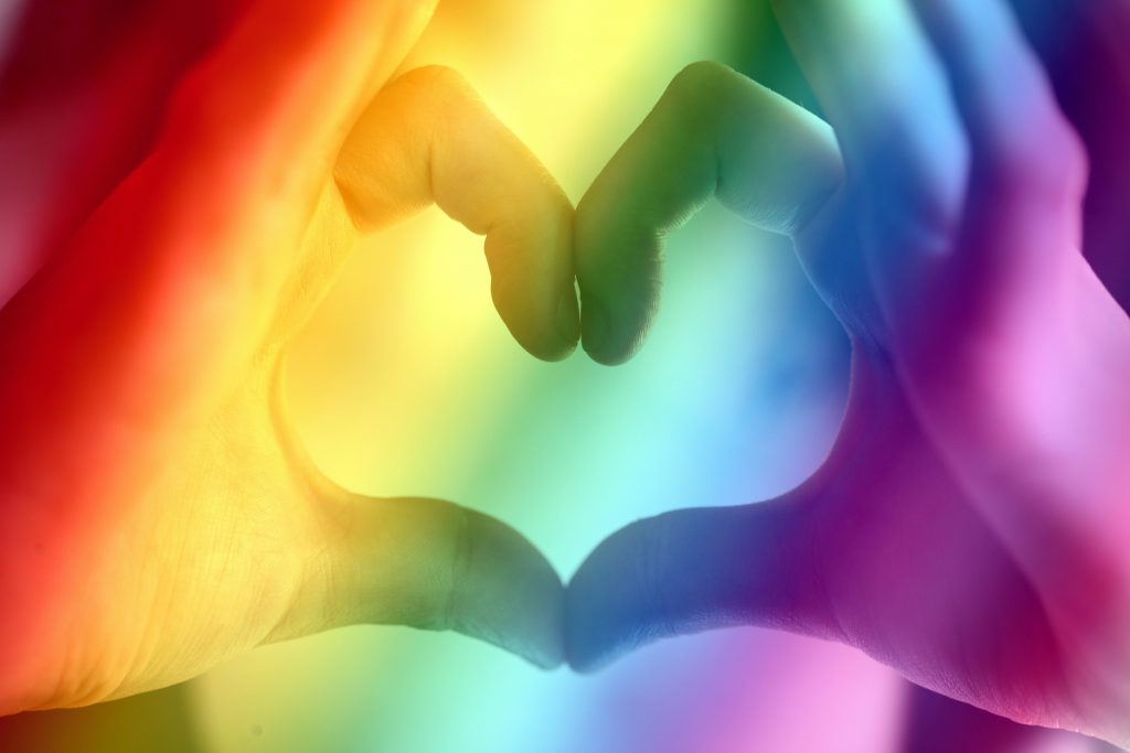 zwei Hände formen ein Herz; darüber liegt ein Regenbogen
