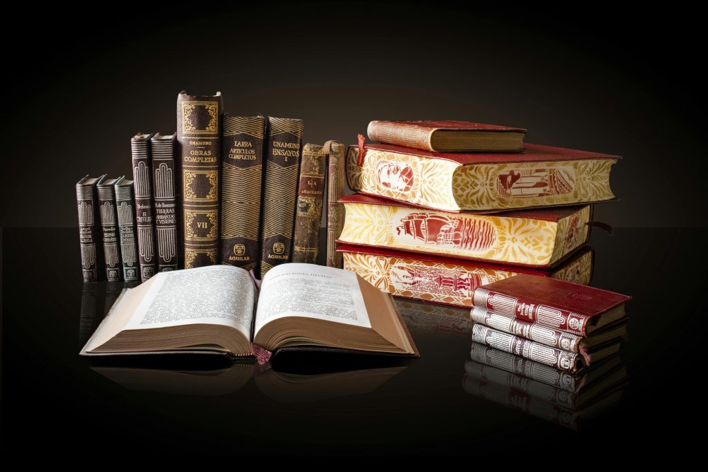 Auf einem dunklen Tisch stehen ein paar älter wirkende Bücher in roten und schwarzen Einbänden.
Eines von ihnen ist aufgeschlagen.