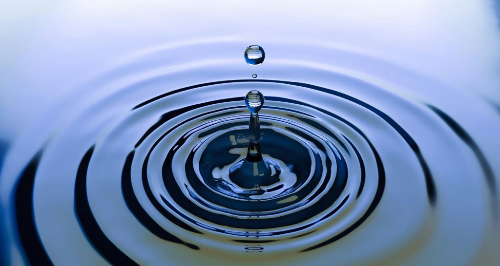 ein Wassertropfen fällt ins Wasser und zieht dabei Kreise