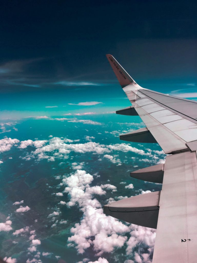 Blick aus einem Flugzeug:
der linke Flügel, darüber dunkelblauer Himmel, darunter türkis, grau und ein paar weiße Wölkchen